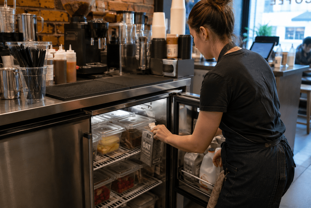 Café worker using under-counter refrigeration during a busy service period